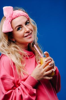 pregnant girl in pink clothes with a bottle of juice on a blue background.