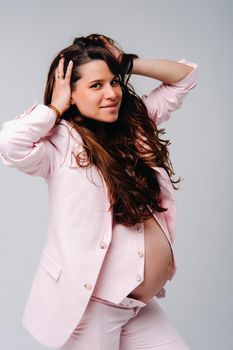 pregnant woman in pink suit close-up on gray background.