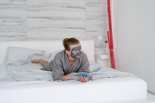 Womens health. Spa and wellness. Woman with face mask relaxing lying on the bed reading a magazine