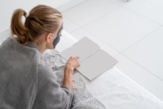 Womens health. Spa and wellness. Woman with face mask relaxing lying on the bed reading a magazine. Mock up design