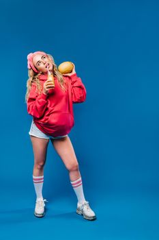 pregnant girl in pink clothes with a bottle of juice and a melon on a blue background.
