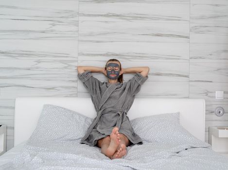 Womens health. Spa and wellness. Woman with face mask relaxing sitting on the bed