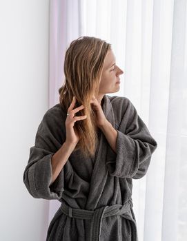 Womens health. Spa and wellness. Happy young woman applying hair mask standing next to the window