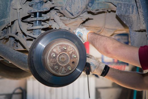 The man's hands detach the worn and rusty rear wheel disc. In the garage, a person changes the failed parts on the vehicle. Small business concept, car repair and maintenance service.