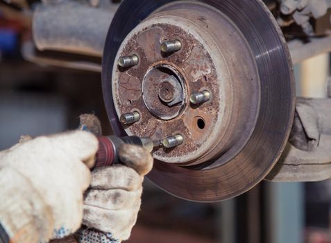 The man's hands are turning the worn out rear brake disc with a screwdriver. In the garage, a person changes the failed parts on the vehicle. Small business concept, car repair and maintenance service