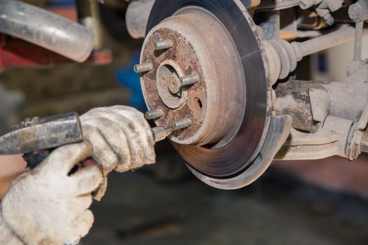 Hands knock off the thread on the bolt of the worn rear hub with a hammer. In the garage, a person changes the failed parts on the vehicle. Small business concept, car repair and maintenance service.