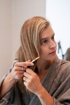 Womens health. Spa and wellness. Young woman in gray bathrobes brushing her hair and smiling while looking at the mirror