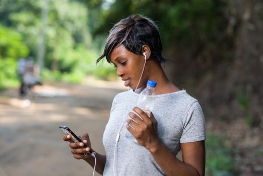 Slim woman athlete holding a bottle of water and using a modern cell phone while jogging outdoors. Sport concept