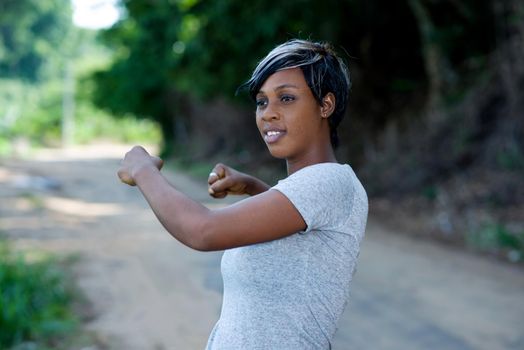 Closeup of a young woman warming her body by stretching her arms before jogging or yoga in the park surrounded by nature and the light of the sky. Concept of health care and sport.