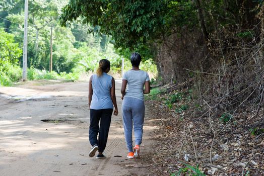 two women running backside along the road in the wilderness doing sports together