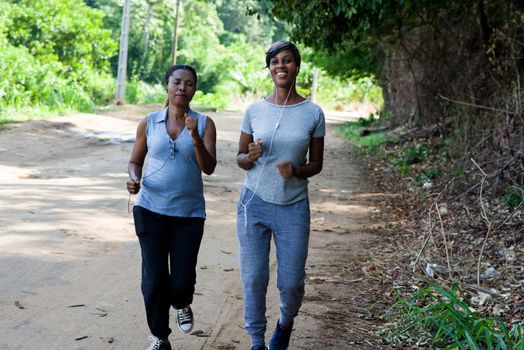 two smiling women with headphones and fitness clothes running along the road doing sports together