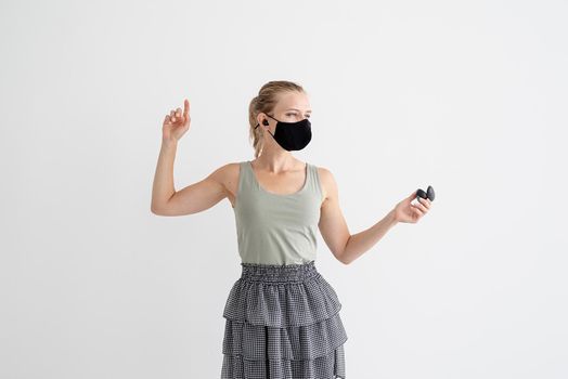 Music, isolation and leisure. Young woman in a protective mask holding wireless earbuds and dancing