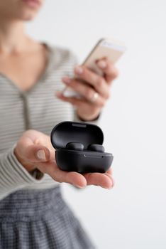 Wireless technology. Young woman holding wireless earbuds operated by the phone