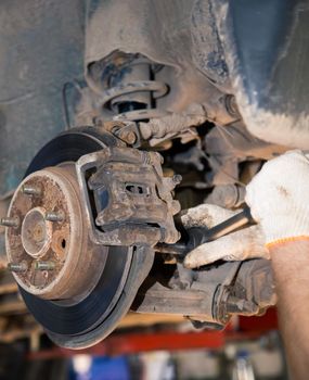 The man's hands unscrew the worn and rusty rear wheel caliper. In the garage, a person changes the failed parts on the vehicle. Small business concept, car repair and maintenance service.