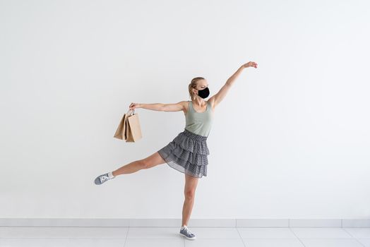 Healthcare and quarantine concept. Young woman dancing ballet with shopping bags in a protective mask.