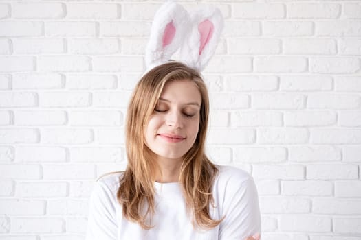 Spring holidays, Easter. Portrait of a happy woman in bunny ears on white brick wall background