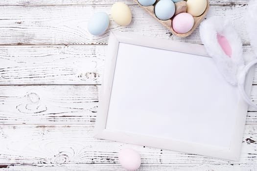 Spring holidays, Happpy Easter. Pastel colored Easter eggs with blank white frame for mockup design on white wooden background
