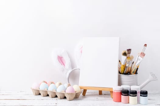 Spring holidays, Happpy Easter. Pastel colored Easter eggs and mimosa flowers with blank white frame for mockup design, front view on white brick wall background