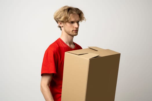 Delivery man holding a cardboard boxes and smiling while standing against white background. Courier holding a cardboard box in front of himself