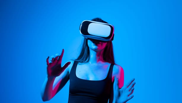 Portrait of brunette woman in a black top with 3D virtual reality glasses enjoys his trip in an adventurous world in neon light. Concept of connection technology with science, augmented reality