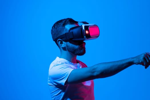 Bearded brunette male in vr glasses plays online, work or study with technology of future, explores virtual world, in neon light. Entertainment and game with modern gadget and 3D simulation