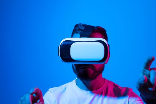 Young man wearing virtual reality goggles and speasing with a friends in the metaverse. Bearded man exploring virtual reality video games in a studio