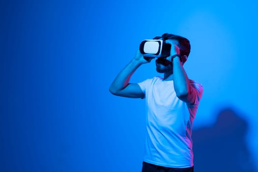 Portrait of young man with 3D virtual reality glasses enjoys his trip in an adventurous world in neon light. Concept of connection technology with science, augmented reality