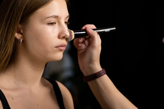 Process of making makeup. Make-up artist working with brush on model face. Portrait of young blonde woman in beauty saloon interior. Applying tone to skin