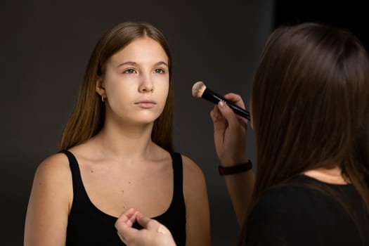 Close up face of beautiful young woman getting powder on her cheek with a brush. Professional makeup artist