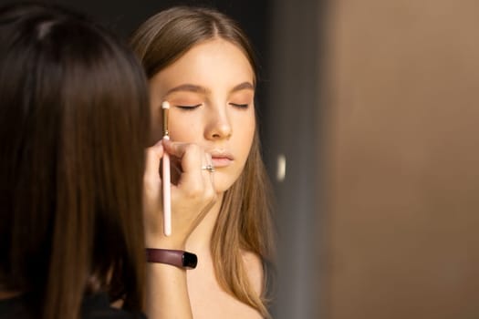 Proffesional make-up artist applying eyeshadow powder on a models eyes in beauty studio
