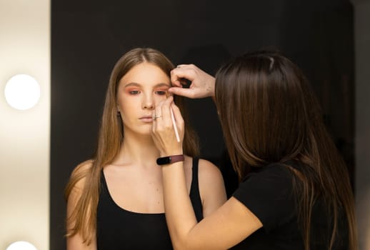 Makeup artist applying liquid tonal foundation on the face of the woman in make up room
