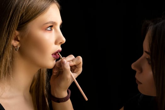 Professional make-up artist applying bright red lipstick on beautiful girl using special lip brush