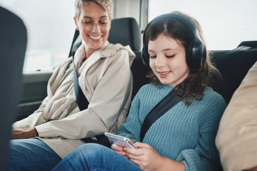 Travel, driving and child with grandmother in car on a smartphone and headphones for transportation or safety belt happiness. Insurance and old woman with kid games using phone mobile app on journey.