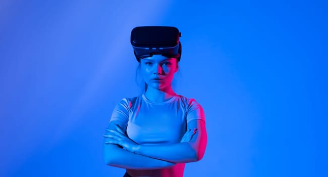 Portrait of young brunette woman gamer with virtual reality headset on a head looks straight in a camera with a hands crossed on a breasts