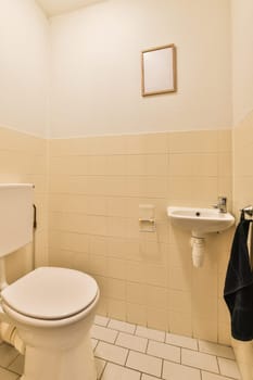 a white toilet and sink in a small bathroom with beige tiles on the walls, along with a black towel