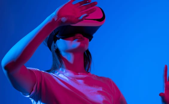 Female gamer entering a game while wearing virtual reality goggles in neon light. Young woman experiencing immersive technology in a studio