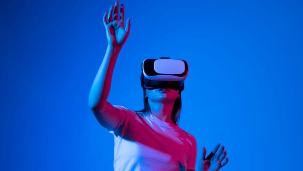 Brunette woman in virtual reality headset playing a video games with a friend's and gesturing with a hands in a neon light. Future gaming concept