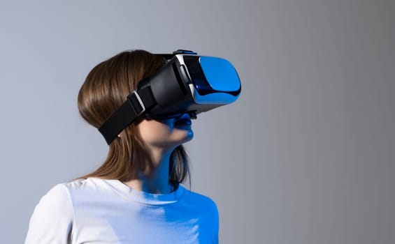 Metaverse concept. Brunette woman in a white t-shirt with vr glass, playing video games with virtual reality headset, trying to touch something with his hand
