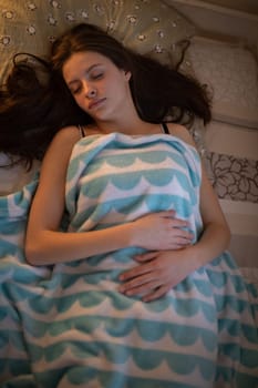 A young girl sleeps in a bed covered with a wool blanket. Top view of a teenage girl with her eyes closed resting while lying on her back.