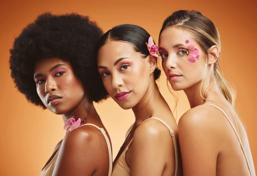 Skincare, flowers and beauty portrait of women in studio for feminism, woman empowerment and cosmetics. Diversity, face and group of beautiful natural models with floral standing by orange background.