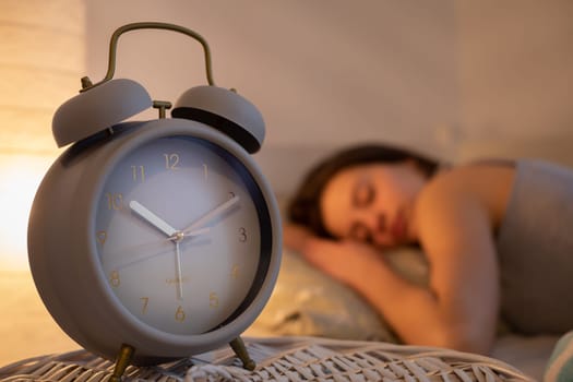 The alarm clock stands on the cabinet next to the bed in which the woman sleeps with the bedside lamp lit. It is already 10 minutes past 10 o'clock on the clock.