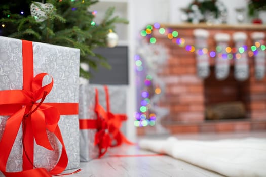 Elegant package on a bright floor. Silver gifts with red ribbons under Christmas tree.