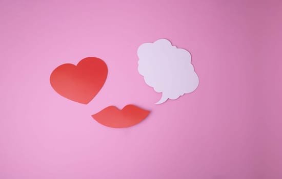 On a pink background paper red lips and a heart and a white cloud for words.