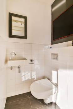 a small bathroom with a toilet and tv above the toilet bowl, in a white tiled wall behind it is a black framed mirror