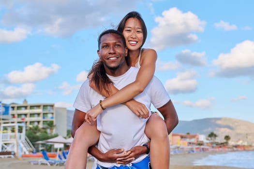 Happy young beautiful couple having fun on beach. Afro american asian couple laughing enjoying vacation in seaside nature. Multicultural, multiethnic family, relationships, togetherness, lifestyle