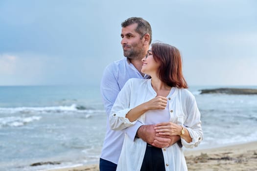 Outdoor portrait of mature couple hugging on beach, background of sea nature, copy space. Middle-aged happy romantic man and woman. Relationships, feelings, lifestyle, marriage, family, people concept