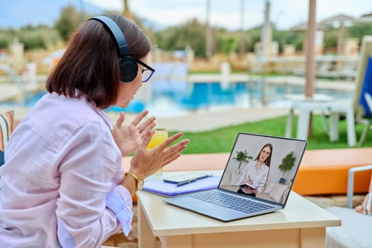 Remote work, business, woman in outdoor headphones at table talking online with young female colleague, client, using laptop. Video conference, videocall, web chat, technology concept