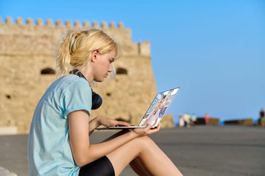 Video call on laptop, teenage friends talking online. Web chat of teenage girl sitting on seashore in European tourist destination and guy. Technology, tourism, friendship, lifestyle, young people concept