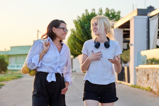 Outdoor portrait of happy mom and teenage daughter walking together in summer in sunset light. Family, communication, motherhood, mother's day, adolescence concept