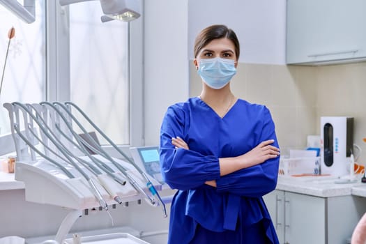 Portrait of confident female dentist doctor in office looking at camera. Young female in medical protective mask in blue uniform, copy space. Dentistry, medicine, health care, profession, stomatology